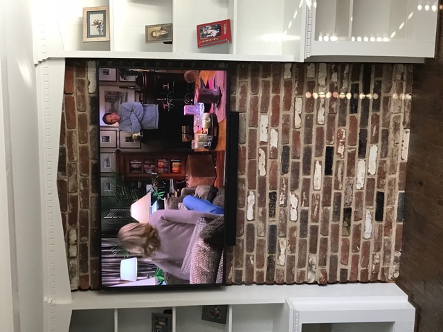 Large TV mounted on brick accent wall between built-in shelves in NJ home